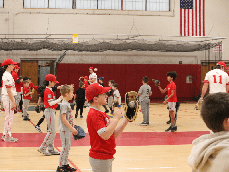 Youth baseball players warming up in a high school gym